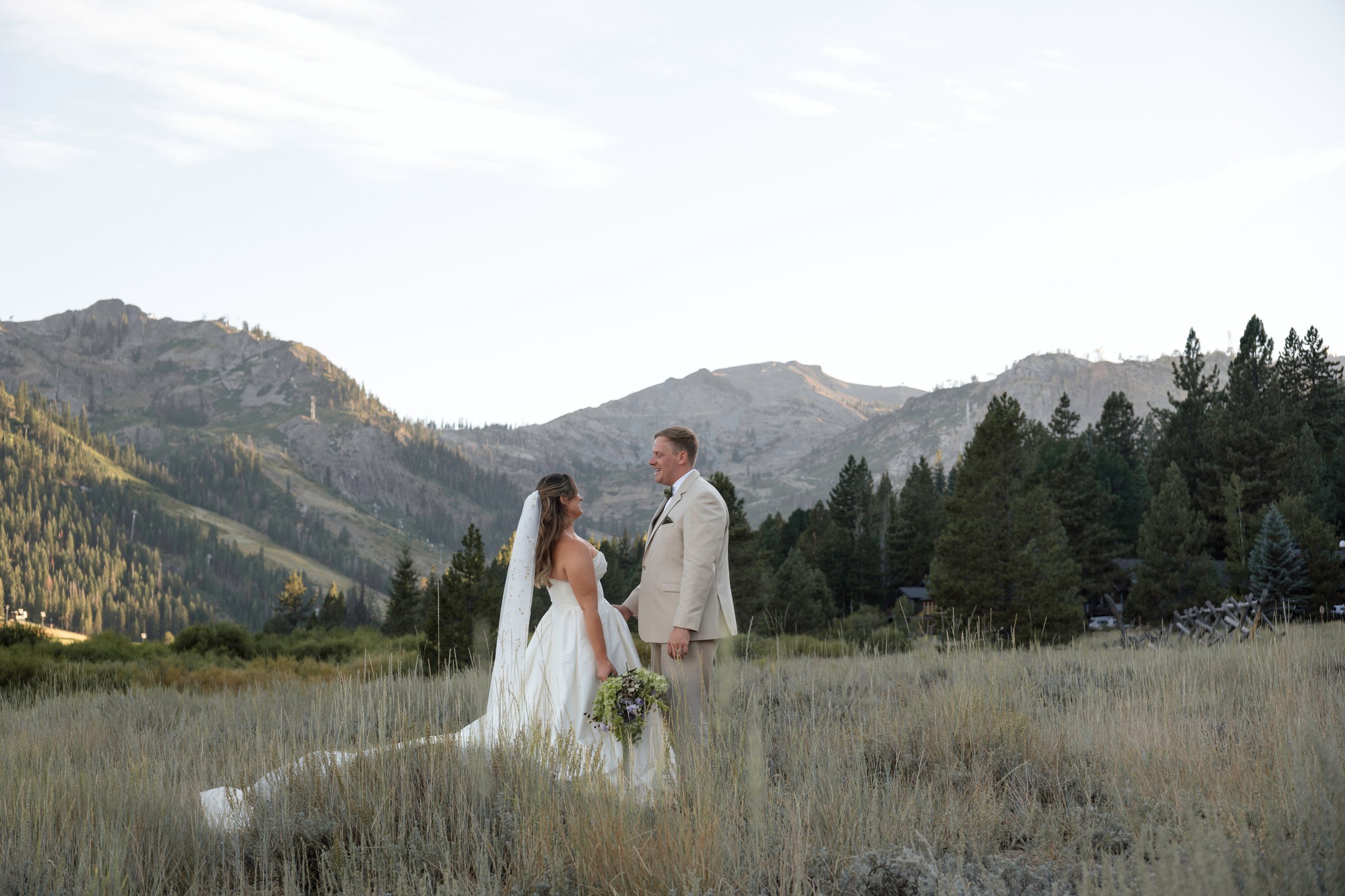 Golden hour in an Olympic Valley meadow: bride and groom in tall grass with the Sierra Nevada behind them, bride holding a green and lavender bouquet